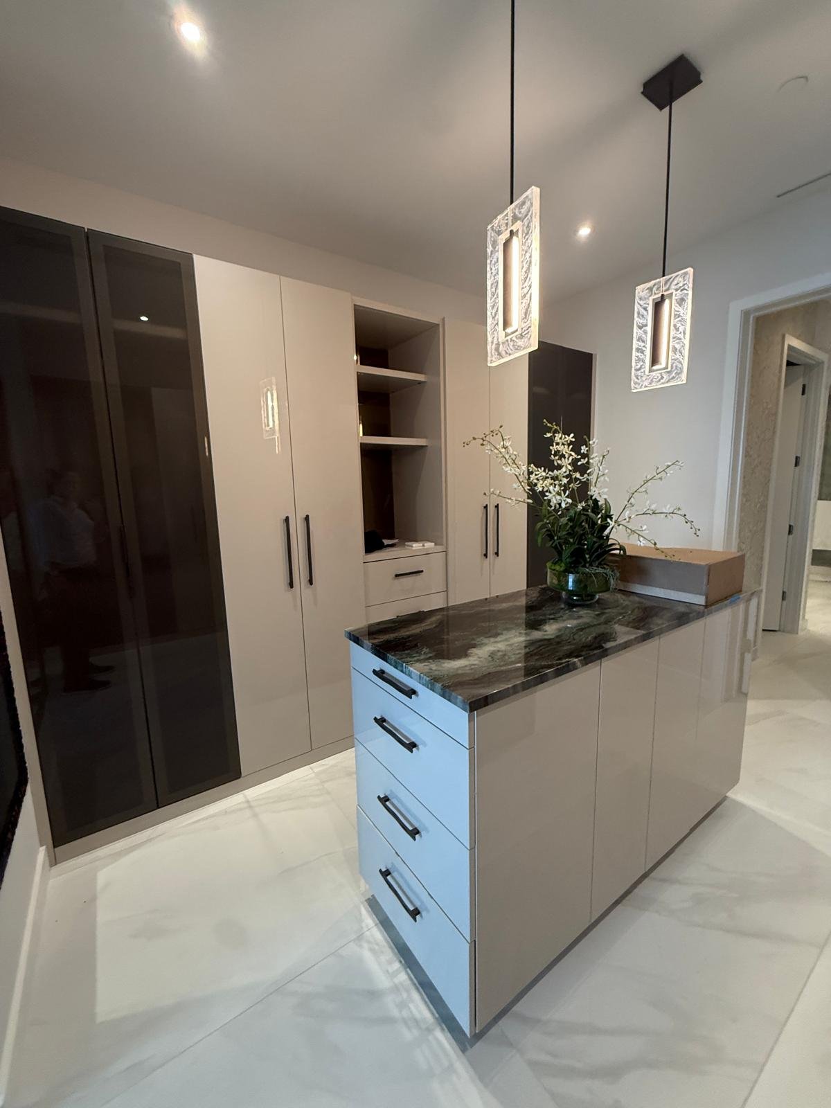 A wardrobe section combining doors that conceal the interior with others that reveal the inner spaces; the stone-topped island offers a functional surface.